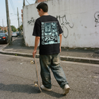 Person wearing a black t-shirt with graphic design, holding a skateboard on an urban street.