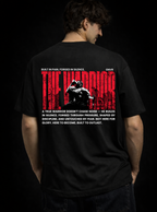 Person wearing a black t-shirt with 'The Warrior' design on the back against a dark background