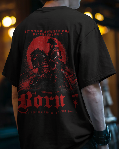 A person shown from the back wearing a black graphic ONVR Oversized T-shirt with a large red and black print featuring the word 'Born' and dramatic artwork, against a blurred warm-toned indoor background.