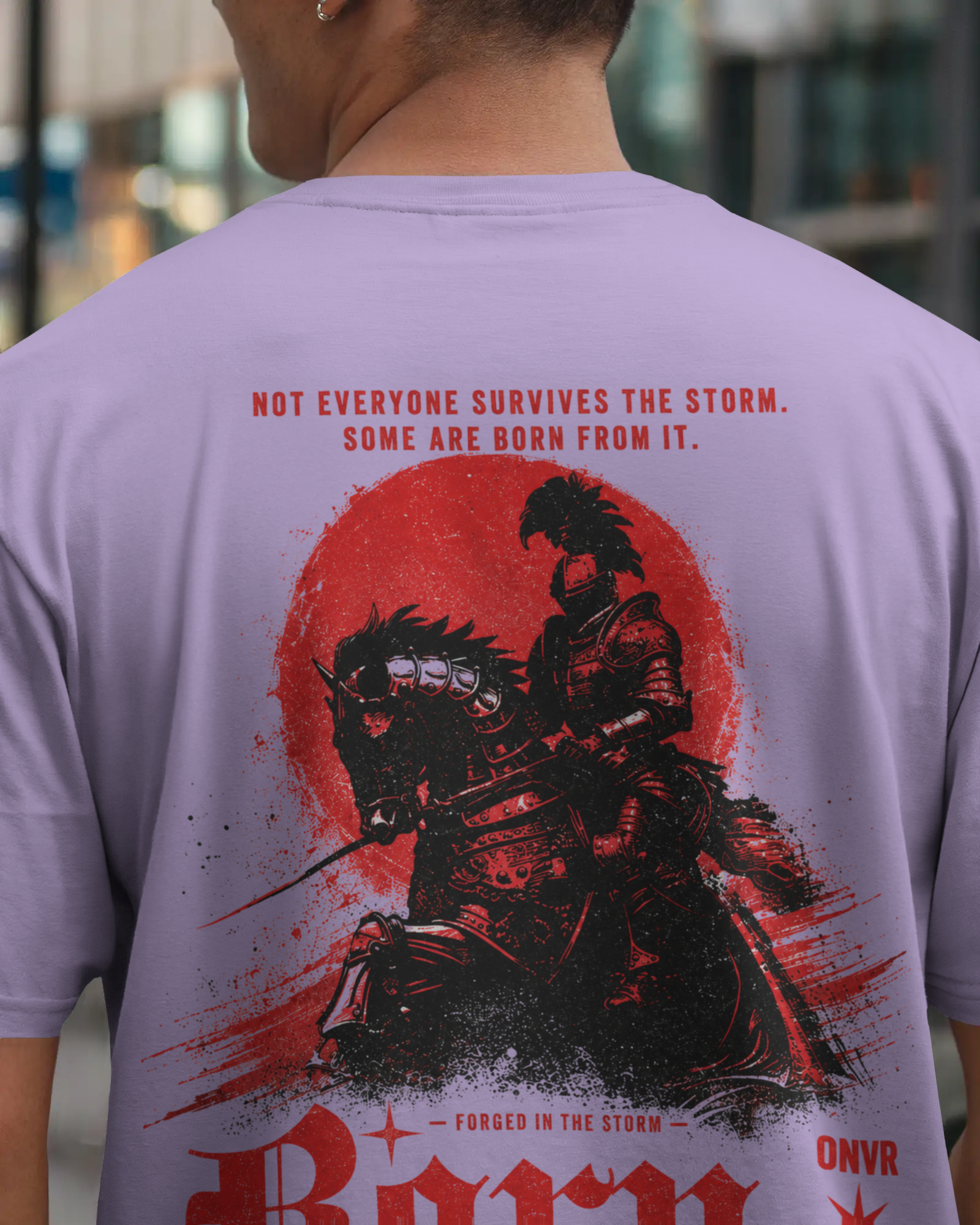 A person shown from behind wearing a light lavender-purple ONVR Oversized t-shirt with a large red and black samurai graphic print on the back, featuring the text 'NOT EVERYONE SURVIVES THE STORM. SOME ARE BORN FROM IT.