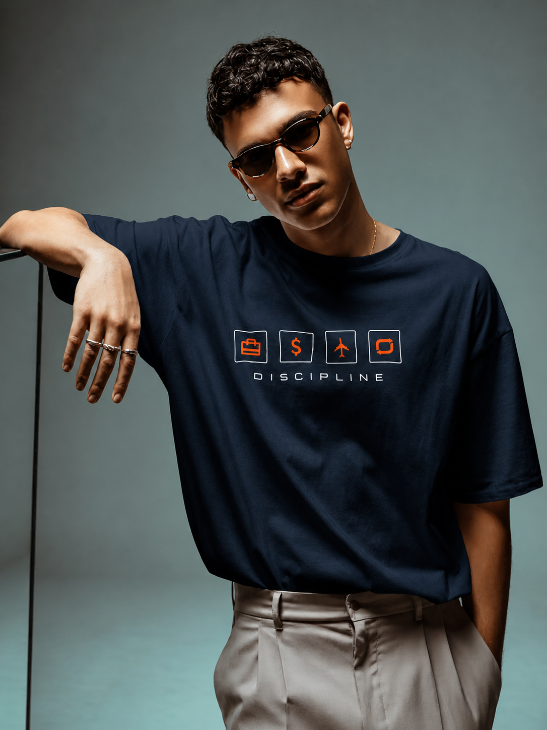 Man wearing a navy blue t-shirt with graphics and text, leaning against a gray background.