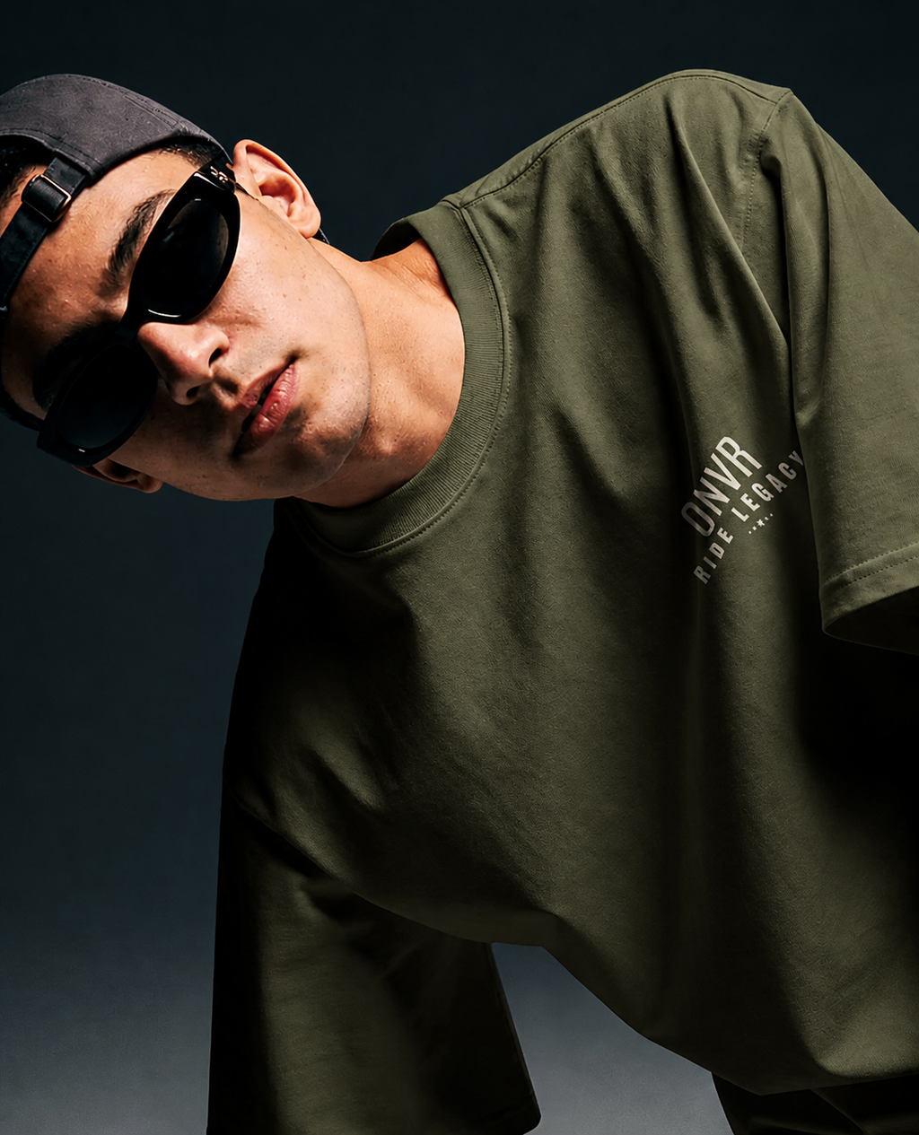 Man wearing a green t-shirt with text and sunglasses against a dark background