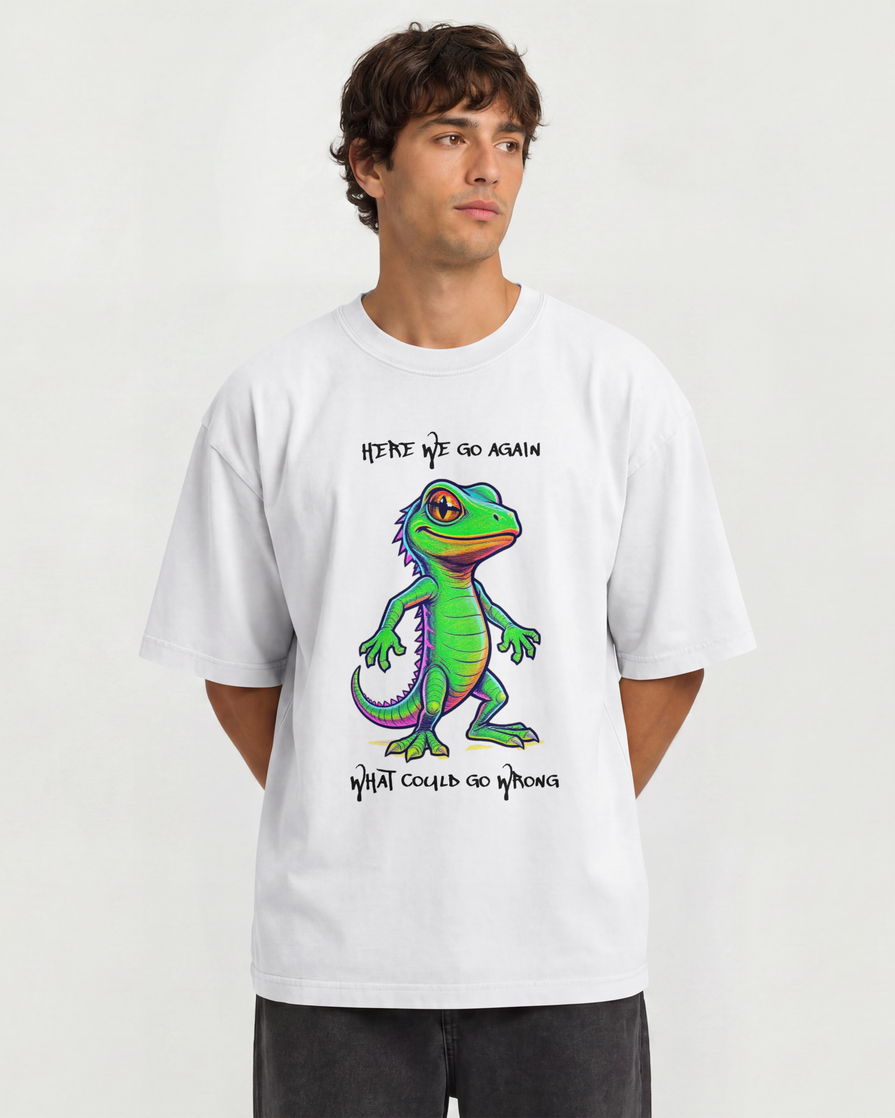 A man wearing a white graphic t-shirt with a colorful cartoon gecko and the text 'HERE WE GO AGAIN' and 'WHAT COULD GO WRONG'.