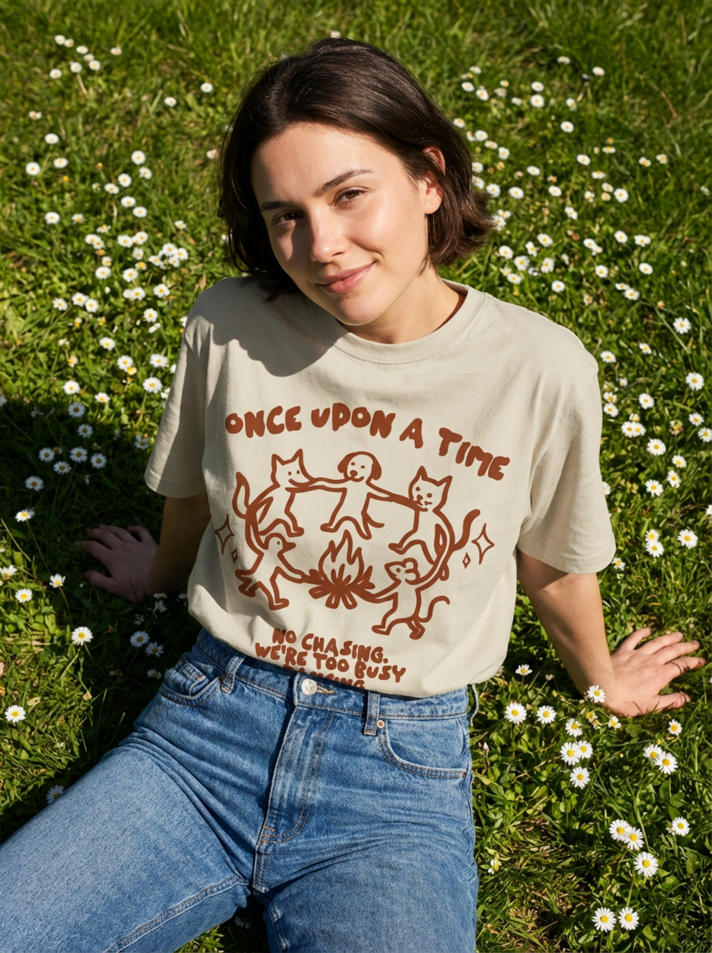 Person wearing a t-shirt with a graphic design in a grassy field with flowers