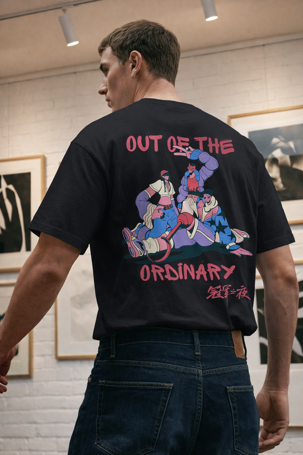 Person wearing a black t-shirt with colorful graphic design and text 'OUT OF THE ORDINARY' in an art gallery.