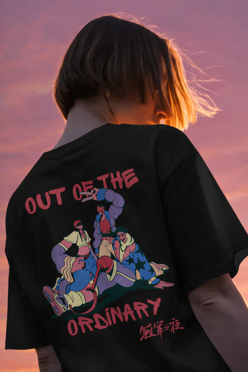 Person wearing a black t-shirt with colorful graphic and text 'Out of the Ordinary' against a pink sunset sky.
