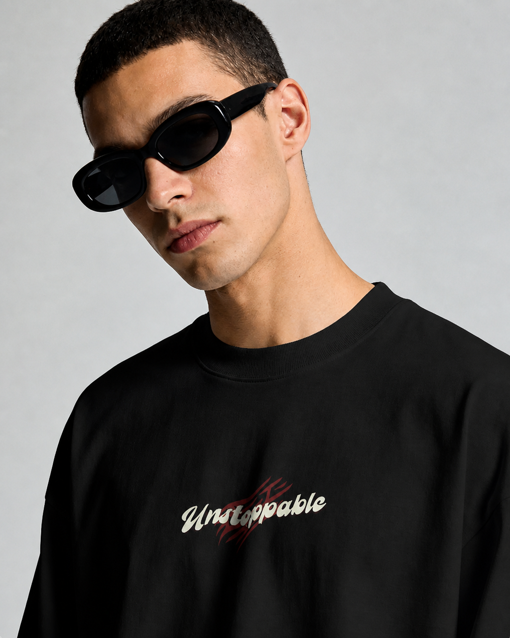 Person wearing a black sweatshirt with 'Unstoppable' text and black sunglasses on a gray background